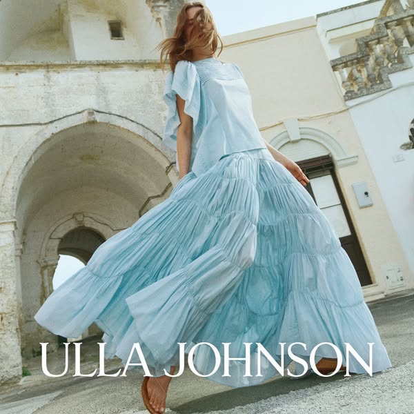 This Ulla Johnson ad showcases a woman in a light blue dress. The shot is angled from below to emphasize the height of t