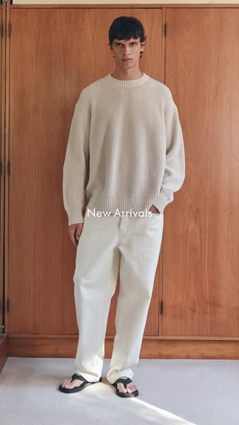 A model is shown wearing a beige knit sweater, white pants, and sandals against a wooden background, with the text &quot