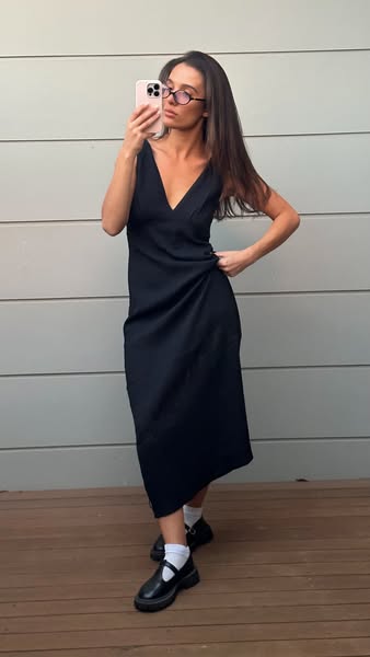 A woman wearing a black dress is taking a selfie with her phone.