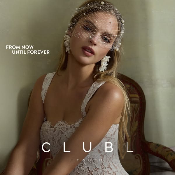 This image ad for Club L London features a woman wearing a lacy white dress and matching pearl-covered headpiece and ear