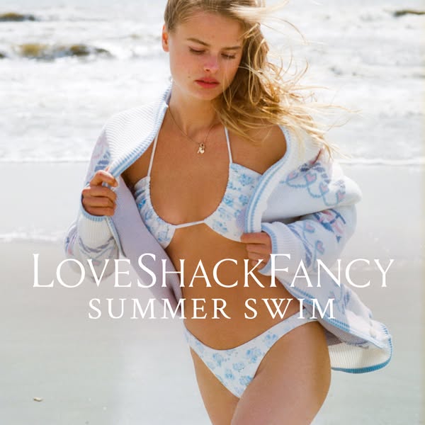An ad for LoveShackFancy's summer swim collection featuring a woman on the beach in a floral print bikini and cardig