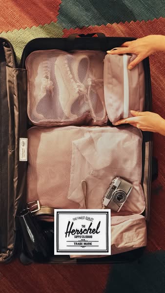 A medium shot of a suitcase with its contents neatly organized using packing cubes and other travel organizers. The bran