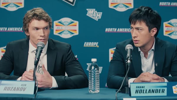 This ad shows two men sitting at a table with mics in front of them and a backdrop with logos. It appears to be a press