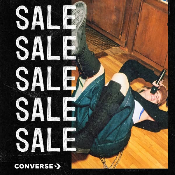 The image is an eye-level shot of a person lying on the floor with their legs up while wearing Converse sneakers. A vert
