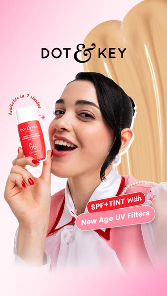 A woman with red nails holds up Dot & Key sunscreen. She has a matching red lip and pink clothing. The sunscreen is