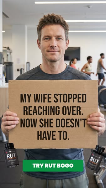A man stands in a gym holding a sign that reads, "MY WIFE STOPPED REACHING OVER. NOW SHE DOESN'T HAVE TO."