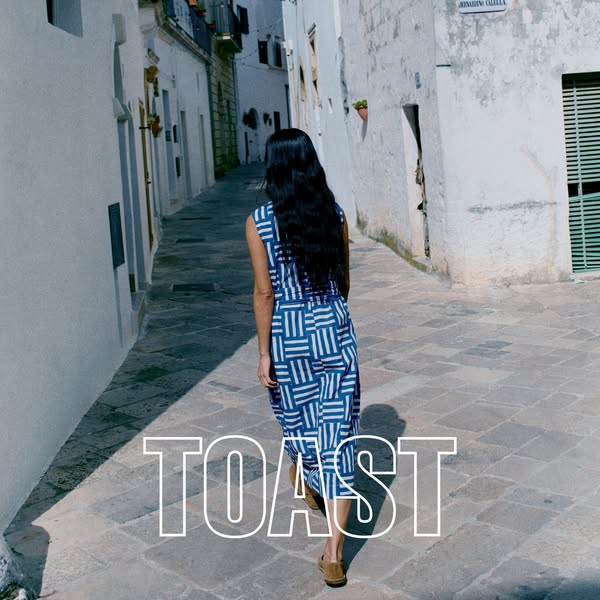 This ad features a woman walking down a narrow street, wearing a blue and white geometric-print sleeveless jumpsuit from