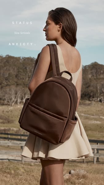 This ad for STATUS ANXIETY shows a woman wearing a beige dress with a brown backpack.