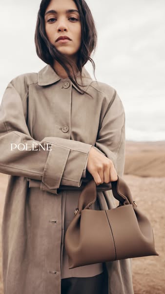 A tan handbag held by a woman wearing a matching colored trench coat. The image highlights the shape of the bag against 