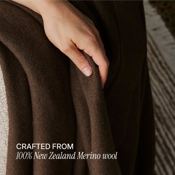 An image ad featuring a brown merino wool garment being held up by a fair-skinned hand to show the quality of its materi