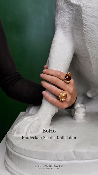 This ad showcases Ole Lynggaard rings from the BoHo collection. A hand adorns two rings while resting on a white dog sta