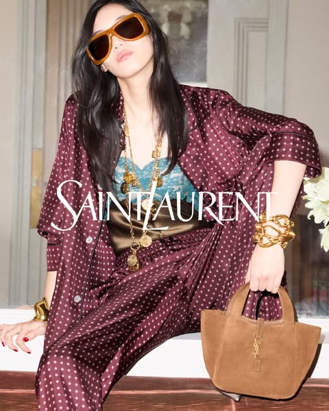 An image ad showcasing a Saint Laurent purse, gold jewlery, and loungewear set on a model in a luxury setting.