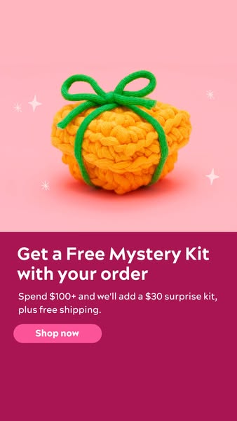This image ad promotes a free mystery kit with orders over $100. The ad features a knitted orange item tied with a green