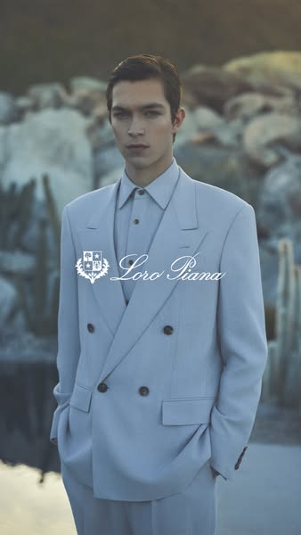 A vertical image ad features a fair-skinned male model wearing a blue suit, standing in front of a stone landscape with 