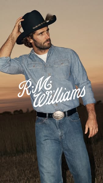 This is a vertical image ad featuring a man in R.M. Williams clothing. He is standing in a field. The company logo is vi