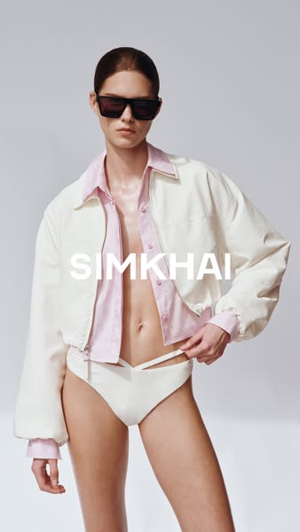 A woman in a two-piece outfit and sunglasses, wearing a jacket, is shown to promote the Simkhai brand.