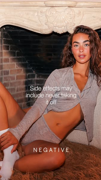 This image ad for NEGATIVE intimates features a young woman lounging in front of a fireplace wearing a matching grey car