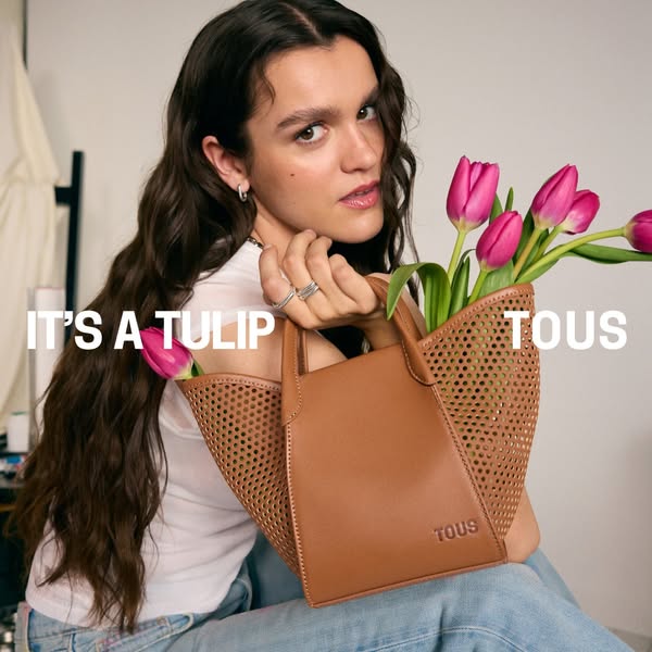This ad for TOUS features a woman holding a small brown leather bag filled with pink tulips. The text overlay states