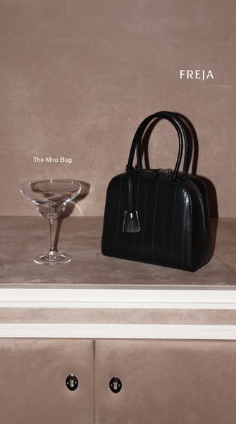 An ad for Freja's Miro Bag, this image features the bag next to a cocktail glass set on a table.
