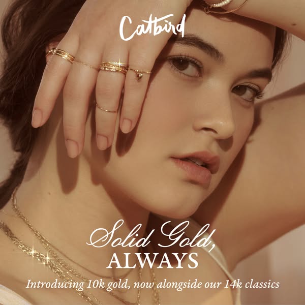 Close up of a woman wearing gold jewelry from Catbird, including rings and necklaces.