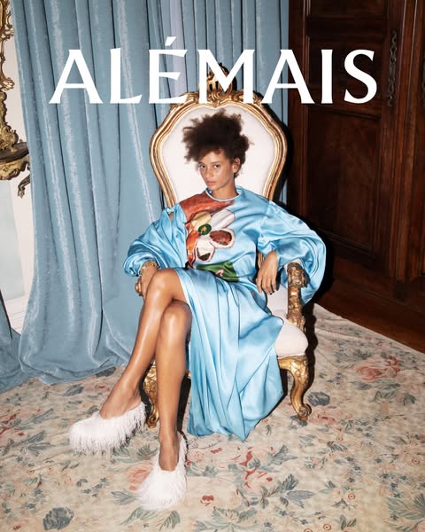 This ad showcases a seated model wearing a blue dress with a floral design. The ad also features a pair of white, feathe