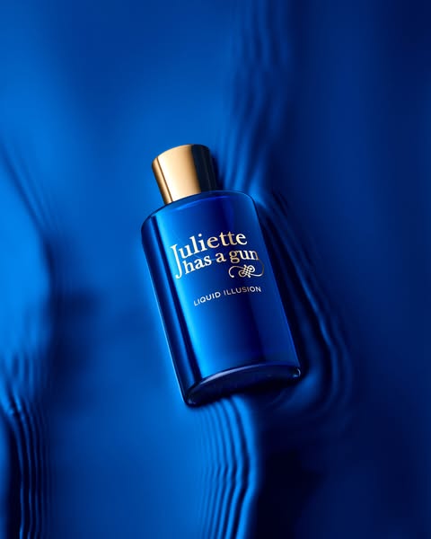This ad showcases the 'Liquid Illusion' perfume from Juliette Has a Gun, set against a vibrant blue backdrop. It