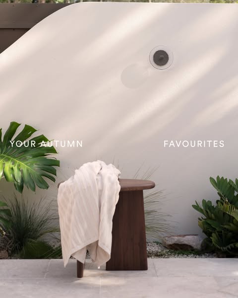 This image ad showcases a cream-colored throw blanket draped on a wooden stool in a sun-drenched outdoor space.