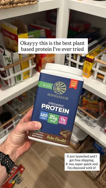 The ad features a hand holding a container of Sunwarrior Organic Protein Dubai Chocolate flavor in front of a stocked pa