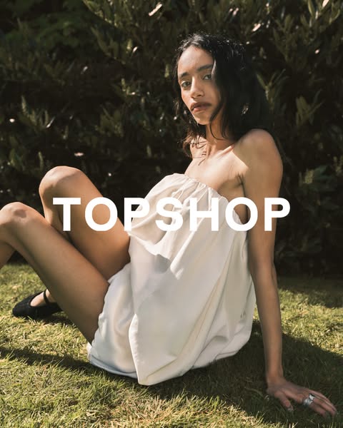 A Topshop ad featuring a model sitting on grass wearing a strapless white dress.