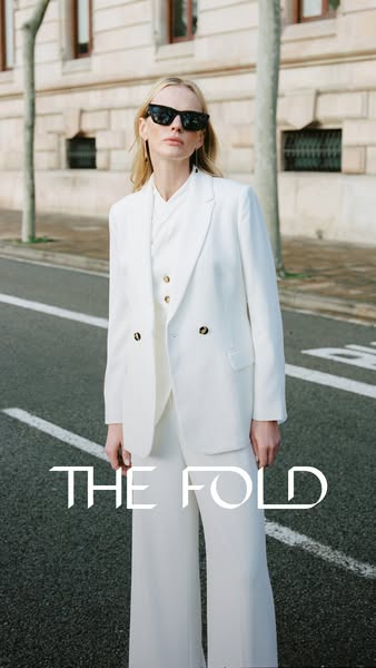 This ad showcases a white suit from The Fold. A blonde woman models the suit outdoors.