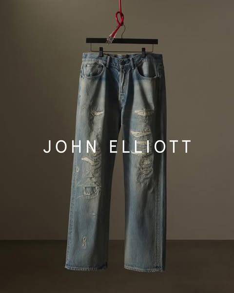 This ad showcases a pair of distressed jeans from the brand John Elliott. The jeans are presented in a simple, well-lit 