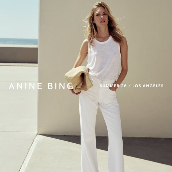 This ad showcases the brand Anine Bing and features a woman wearing a white tank top and white wide leg pants. The backg
