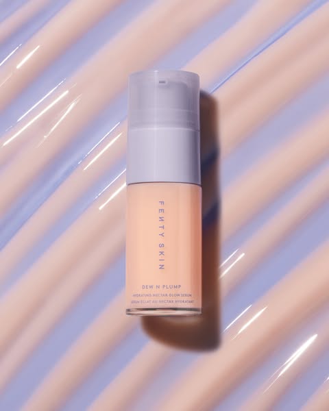 This ad features Fenty Skin's Dew N Plump Hydrating Nectar Glow Serum. The product is displayed against a glossy, te