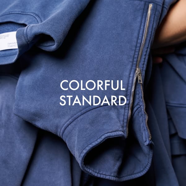 This image ad showcases a blue zip-up sweatshirt from Colorful Standard. The brand name appears in the center of the ima