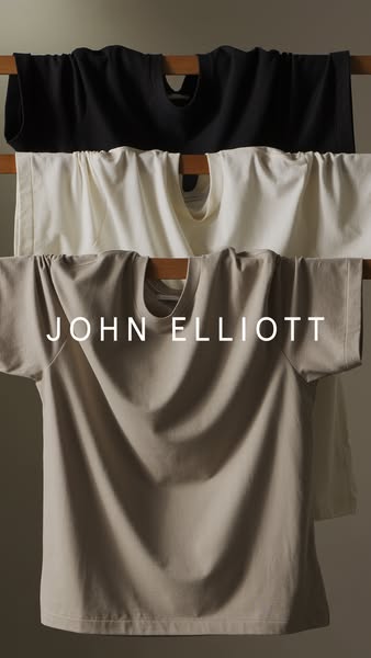This ad showcases three John Elliott t-shirts in different colors hanging on a wooden rack. The brand name is displayed 
