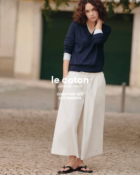 This image ad from Comptoir des Cotonniers features a young woman wearing a navy blue V-neck sweater and white, wide-leg