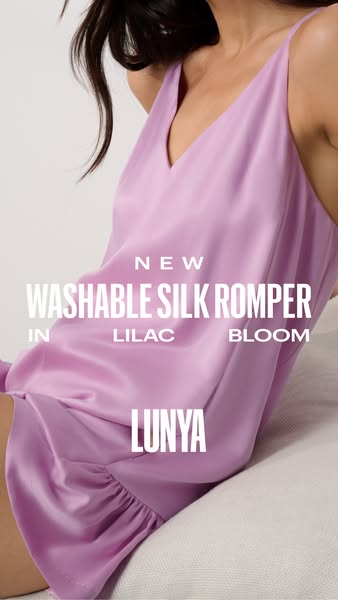 Ad for Lunya's washable silk romper in a lilac bloom color. The ad features a woman lounging in the silk romper, hig