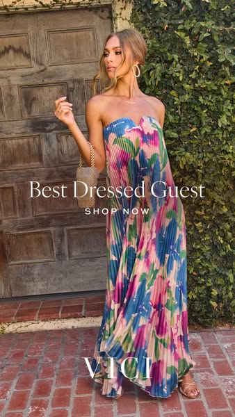 This image ad features a woman modeling a long, floral-patterned dress from VICI, accessorized with jewelry and a small 