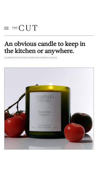 This ad features a Flamingo Estate Roma Heirloom Tomato Candle in a green jar, positioned alongside several tomatoes and