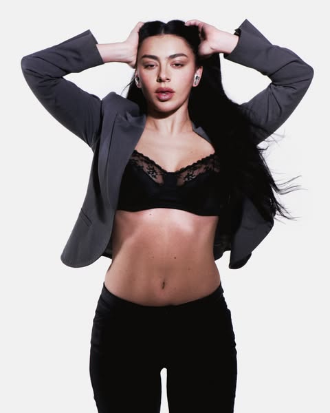 This ad features an image of Charli XCX wearing wireless earbuds. She is posed provocatively wearing a blazer with a bra