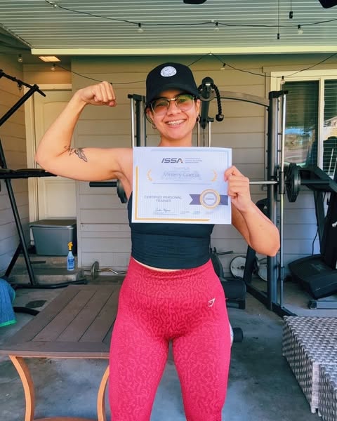 This image ad features a woman holding her personal trainer certification from ISSA while flexing her arm. The ad is lik