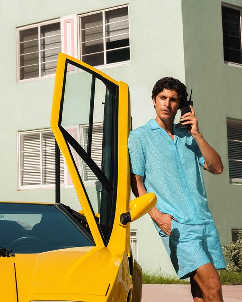 This ad features a man in a matching shirt and shorts set, leaning against a yellow sports car while talking on a vintag