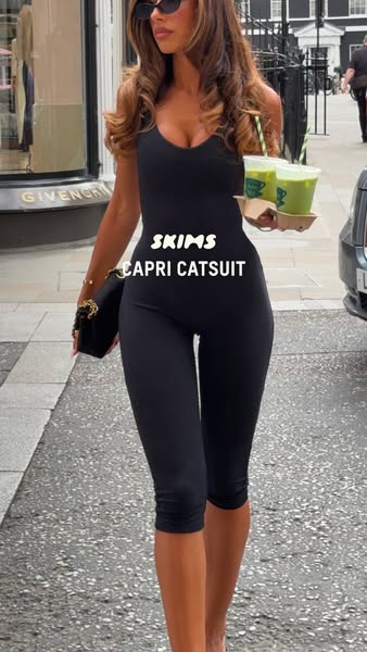 This ad features a woman wearing a black SKIMS Capri Catsuit while walking down a city street. She is holding two green