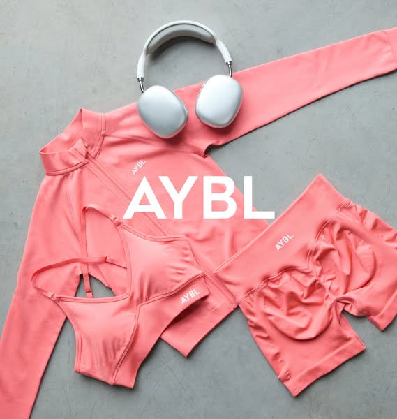 This ad showcases a matching set of AYBL activewear in a flat lay composition. The set includes a long-sleeve zip-up jac