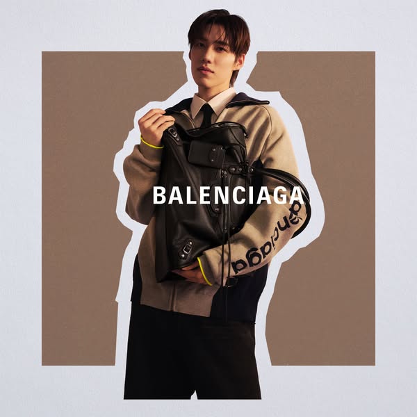 This is an image ad for Balenciaga featuring an Asian man wearing a suit under a cardigan and carrying a Balenciaga bag.