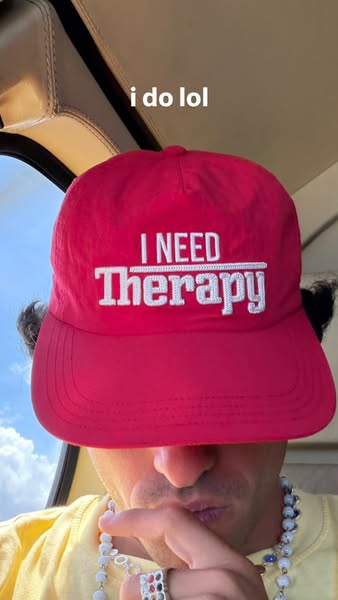 The ad features a person wearing a red hat with white lettering that says 'I NEED Therapy' and the phrase 'I