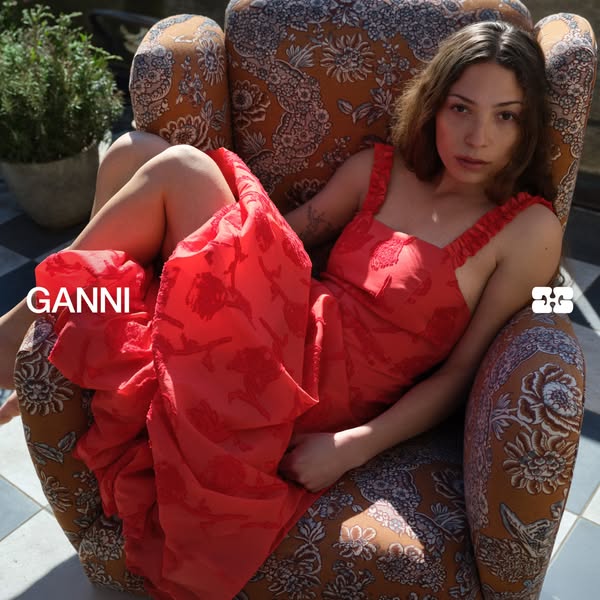 This ad features a woman lounging in a chair wearing a GANNI red floral patterned dress. The ad spotlights the brand GAN