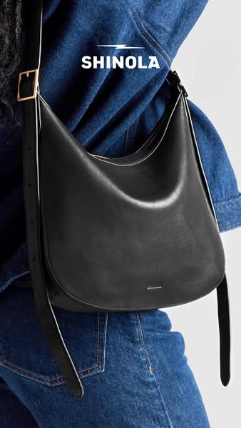 This is a product shot of a black leather Shinola hobo bag being worn by a person in a denim jacket. The bag is the prim