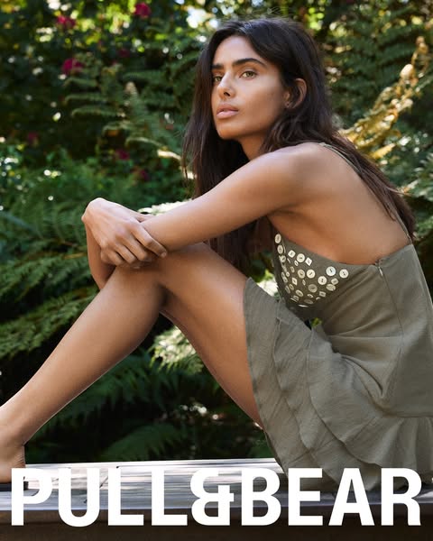 A woman is shown outdoors, sitting with her legs folded in a dress and the brand's logo at the bottom.