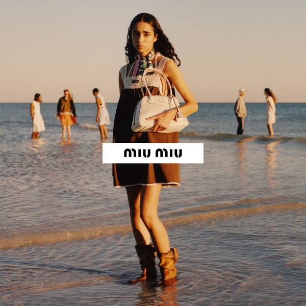 This Miu Miu ad features a woman standing in shallow ocean water, wearing a brown dress and boots, and carrying a small 